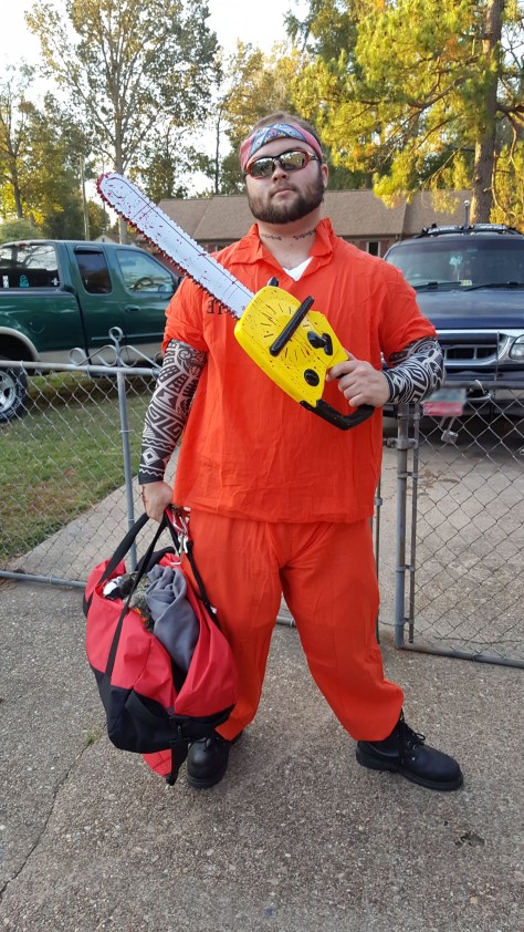 man dressed in orange confict jumpsuide holding toy chainsaw