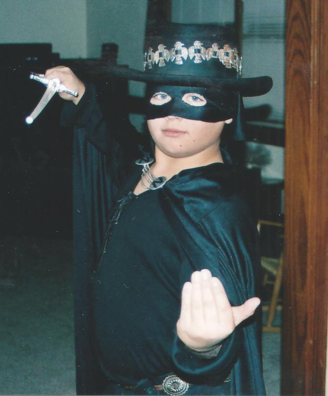 Child dressed a zoro with black hat, clothing and mask holding a sword